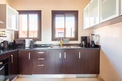 a kitchen with wooden cabinets and a sink and two windows at Marrakech flat with swimming pool & sunny garden in Marrakech