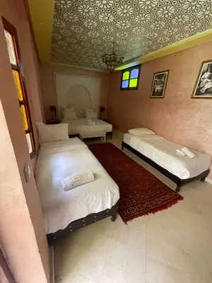 a room with two beds and a table and windows at Riad Naffar in Marrakech