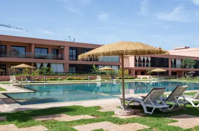 a resort with a swimming pool with chairs and a straw umbrella at Elegance and Serenity at Noria Golf and Pool view in Marrakech