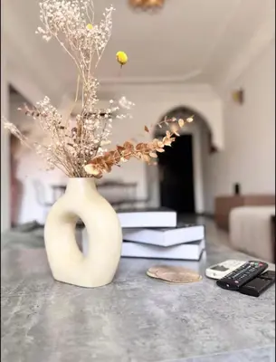 a white vase with flowers on a table with books at Appart hôtel avec piscine in Marrakech