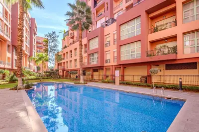 a swimming pool in front of a building with palm trees at Duplex Le Majorelle, Res devant le jardin, piscine in Marrakech