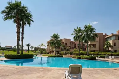 a chair in front of a swimming pool with palm trees at apartment sur GOLF prestigia avec piscine in Marrakech