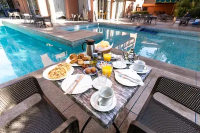 a table with breakfast food next to a swimming pool at Hotel Le Grand Imilchil in Marrakech