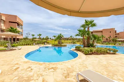 a pool at a resort with an umbrella and palm trees at Luxury Garden-Level Apartment with Poolside Serenity in Marrakech