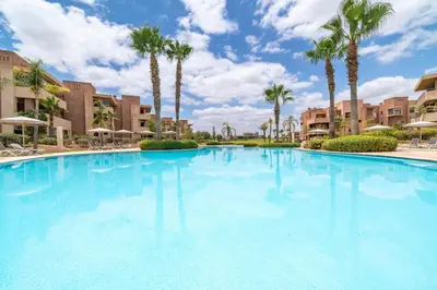 a large swimming pool with palm trees and buildings at Apart Confort Rez-de-Jardin Piscine Wi-Fi Terrasse in Marrakech