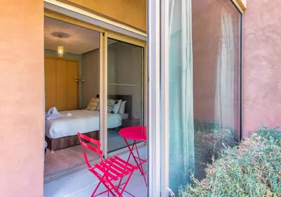 a balcony with two red chairs and a bed at Apart Confort Rez-de-Jardin Piscine Wi-Fi Terrasse in Marrakech