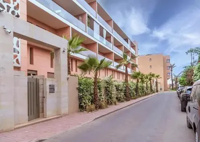 an empty street in front of a building with palm trees at Bel appartement à Marrakech dans la résidence Pearl Garden avec piscine située sur la route de Casablanca Sa grande terrasse a une splendide vue sur la ville et les montagnes de l'Atlas A quelques minutes du centre ville et du grand Stade de Marrakech in Marrakech