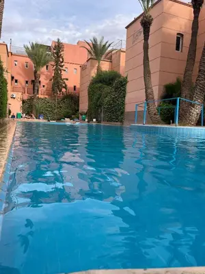 a large blue swimming pool with palm trees and buildings at RIAD Marrakech zina in Marrakech