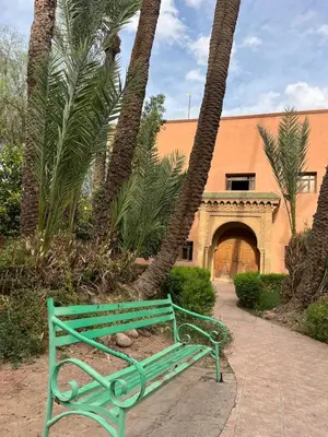 a green bench in front of a building with palm trees at RIAD Marrakech zina in Marrakech
