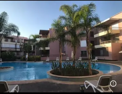 a swimming pool with chairs and palm trees in front of a building at Appartement familial in Marrakech
