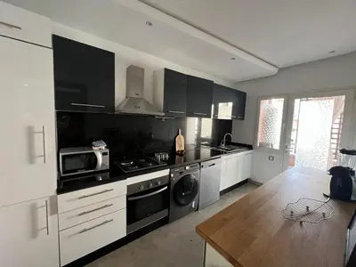 a kitchen with black and white appliances and a wooden table at Appartement familial in Marrakech