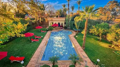a pool in a yard with red chairs and umbrellas at Charming Luxury Villa - Pool & Hot Tub in Marrakech