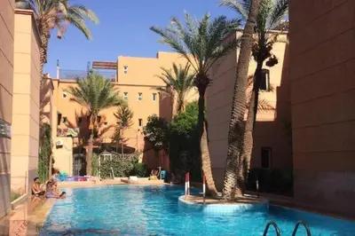 a swimming pool with palm trees and people sitting in it at Said MM in Marrakech