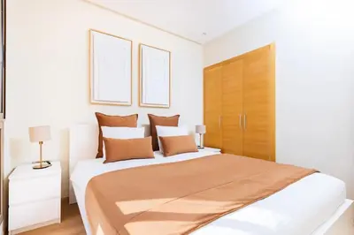 a white bedroom with a large bed with brown pillows at Appartement prestigia golf accès piscine in Marrakech
