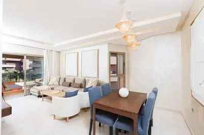 a living room with a table and blue chairs at Appartement prestigia golf accès piscine in Marrakech