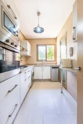 a large kitchen with white cabinets and a sink at Front de piscine en rez de Jardin a Prestigia in Marrakech