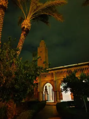 a building with a clock tower and a palm tree at APPARTEMENT DAR MARRAKECh G27 N7 in Marrakech