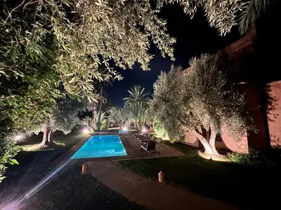 a swimming pool at night with trees and lights at Villa kasbah de luxe, piscine et jacuzzi chauffés, jardin tropical in Marrakech