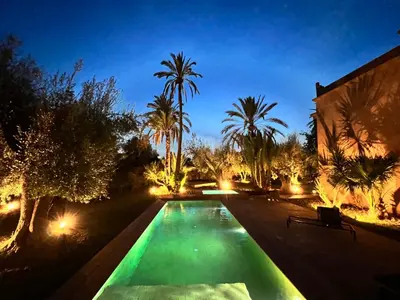 a swimming pool at night with palm trees and lights at Villa kasbah de luxe, piscine et jacuzzi chauffés, jardin tropical in Marrakech