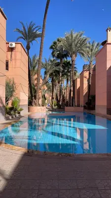 a large swimming pool with palm trees and a building at Riad elmansouri in Marrakech