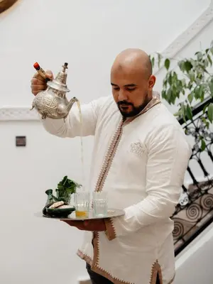a man holding a tea kettle with glasses on a tray at Riad Privatif avec Personnel et Services Exclusifs - Kasbah Boma Marrakech I in Marrakech