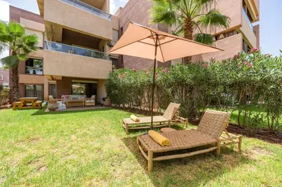 a patio with two chairs and an umbrella in front of a building at Trois chambres et Jardin Prive a Prestigia in Marrakech