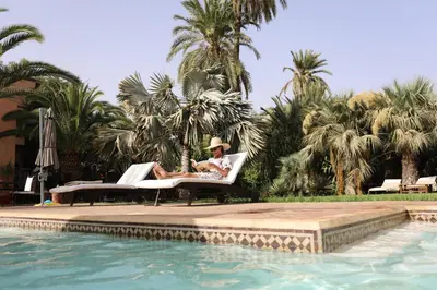 a man sitting in a chair next to a swimming pool at Villa Le Perroquet Bleu in Marrakech