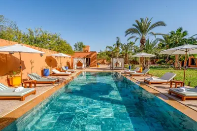 a swimming pool with lounge chairs and umbrellas at Villa Simari Palmeraie Marrakech NOUVEAU! Petit déjeuner compris-Entièrement rénovée-Superbe piscine privée chauffée-Personnel de maison inclus-Grand jardin de 2000m2-Terrain de pétanque-Ambiance typique berbère-Havre de paix in Marrakech