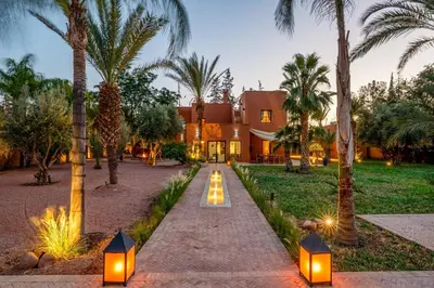a house with palm trees and lights in front of it at Villa Simari Palmeraie Marrakech NOUVEAU! Petit déjeuner compris-Entièrement rénovée-Superbe piscine privée chauffée-Personnel de maison inclus-Grand jardin de 2000m2-Terrain de pétanque-Ambiance typique berbère-Havre de paix in Marrakech