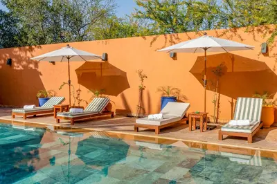 a pool with chairs and umbrellas next to a building at Villa Simari Palmeraie Marrakech NOUVEAU! Petit déjeuner compris-Entièrement rénovée-Superbe piscine privée chauffée-Personnel de maison inclus-Grand jardin de 2000m2-Terrain de pétanque-Ambiance typique berbère-Havre de paix in Marrakech