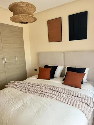 a bedroom with a bed with white sheets and orange pillows at Appartement Cosy - vue Piscine - Prestigia JADE in Marrakech