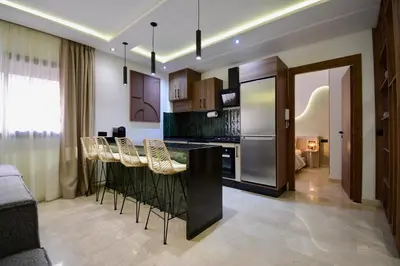 a kitchen with a bar with stools and a refrigerator at Appartement Cosy et Moderne Accès 4 piscines in Marrakech