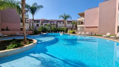 a swimming pool in a resort with palm trees and buildings at Luxueux appartement à Riad Garden in Marrakech