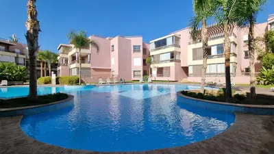 a swimming pool with palm trees in front of a building at Luxueux appartement à Riad Garden in Marrakech