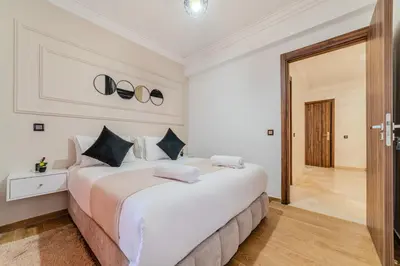 a white bedroom with a large white bed with black pillows at New! Apartment Gueliz 2 min M Avenue with Pool and 24h Security & Parking in Marrakech