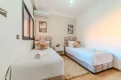 two beds in a bedroom with white walls and wood floors at New! Apartment Gueliz 2 min M Avenue with Pool and 24h Security & Parking in Marrakech