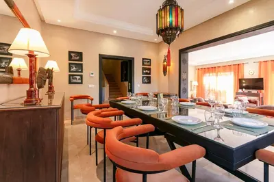 a dining room with a long table and orange chairs at Amelkis Golf Marrakech, Villa 6ch, piscine chauffée in Marrakech
