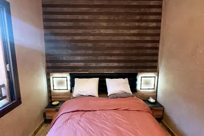 a bedroom with a bed with two nightstands and a wooden wall at Atlas Gardens Apartment in Sraghna
