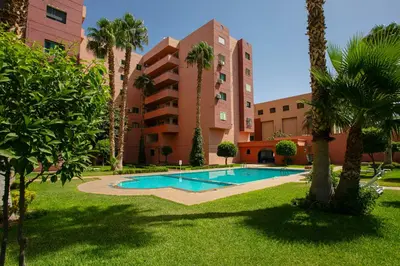 a swimming pool in front of a building with palm trees at Artisan's Hideaway Marrakech in Marrakech