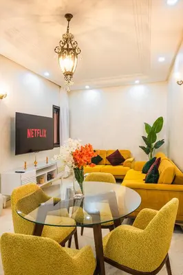 a living room with a glass table and yellow chairs at Appartement Bien équipé au Centre ville Garage Privé et Climatiseur Fibre 5G in Marrakech