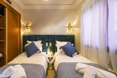 two beds in a small room with blue pillows at Appartement Bien équipé au Centre ville Garage Privé et Climatiseur Fibre 5G in Marrakech