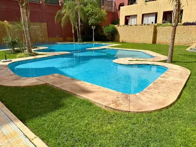 a swimming pool with blue water in the grass at Somptueux Appartement avec Jacuzzi Privé Marrakech in Marrakech