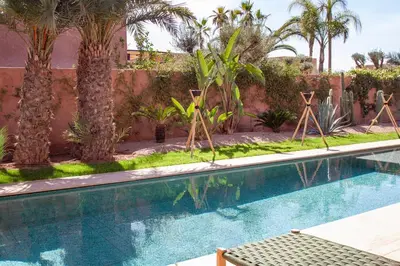 a swimming pool with palm trees and a wall at Villa à Marrakech 8 Personnes, Piscine et Petits-Déjeuners Inclus in Sraghna