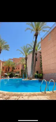 a swimming pool with palm trees in front of a building at Riad abdel in Marrakech
