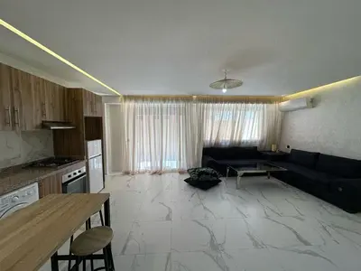 a living room with a black couch and a kitchen at Spacieux Appartement avec terrasse coeur de Marrakech in Marrakech