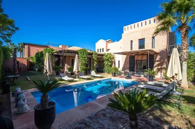a pool in front of a house with palm trees and umbrellas at Amelkis golf villa 3 ch private pool in Marrakech