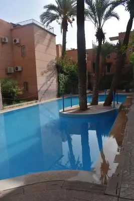 a swimming pool with palm trees and a building at Riad Zaitone 134 in Marrakech
