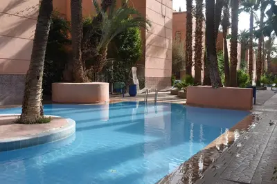 a swimming pool with palm trees and a building at Riad Zaitone 134 in Marrakech