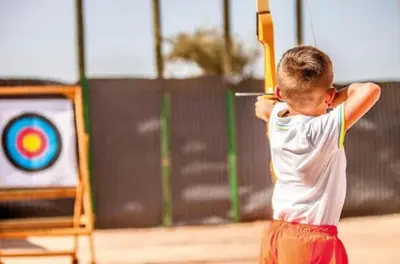 a young boy holding a bow and arrow in front of a target at Appartement Cosy avec Parc et Piscine pour femme in Marrakech