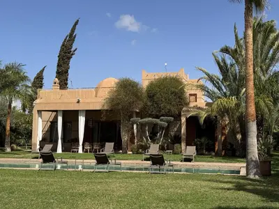 a house with chairs in a park with palm trees at Villa Hilin - Piscine chauffée et hammam privé proche des golfs et du centre ville in Marrakech